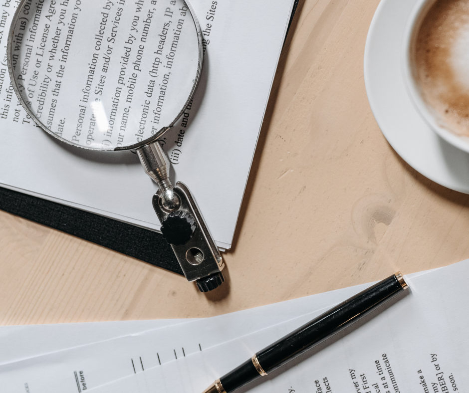 Verträge liegen auf einem Tisch, daneben Lupe, Stift und Kaffeetasse
