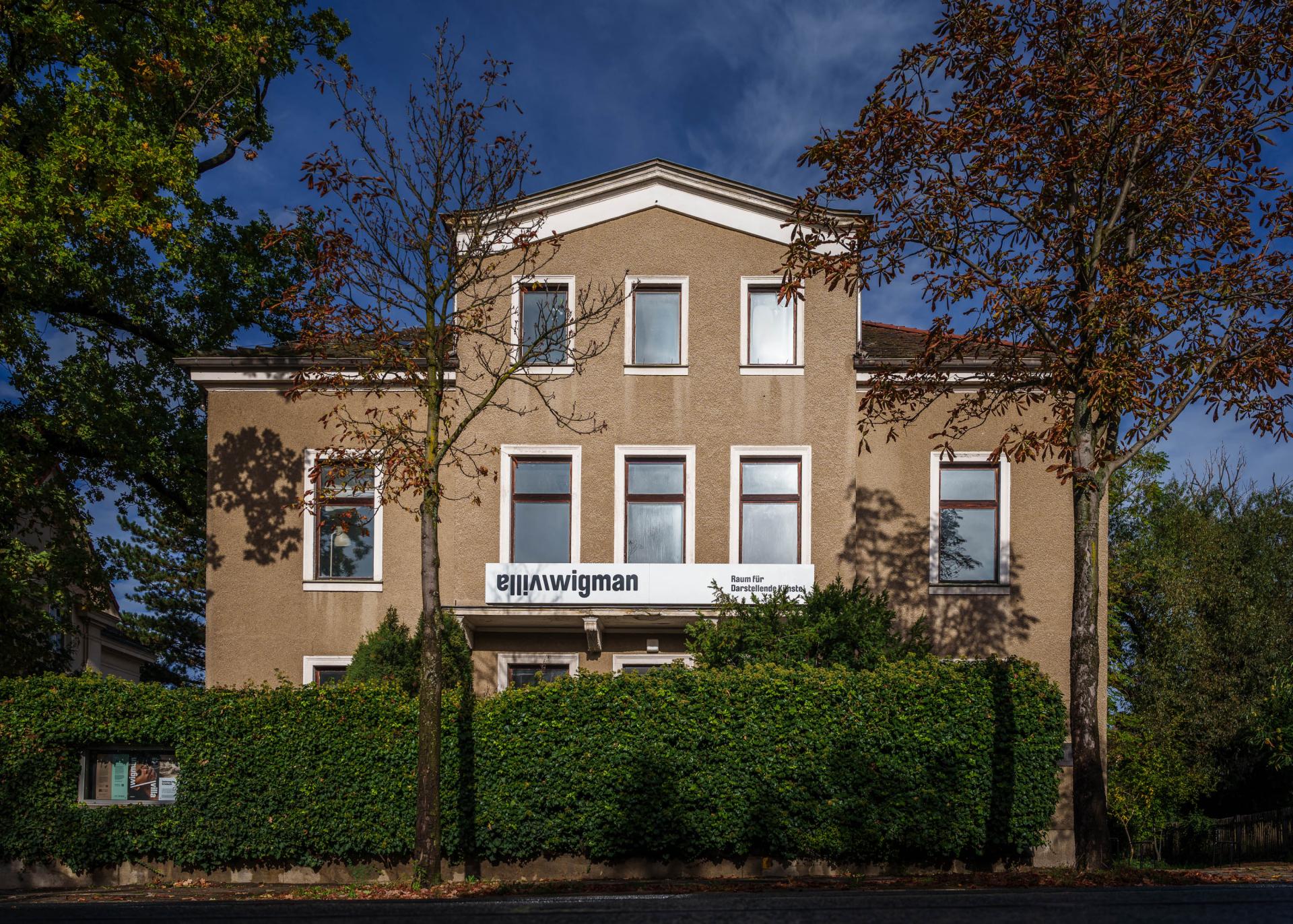 Exterior view of Villa Wigman, gray-brown facade surrounded by green hedges