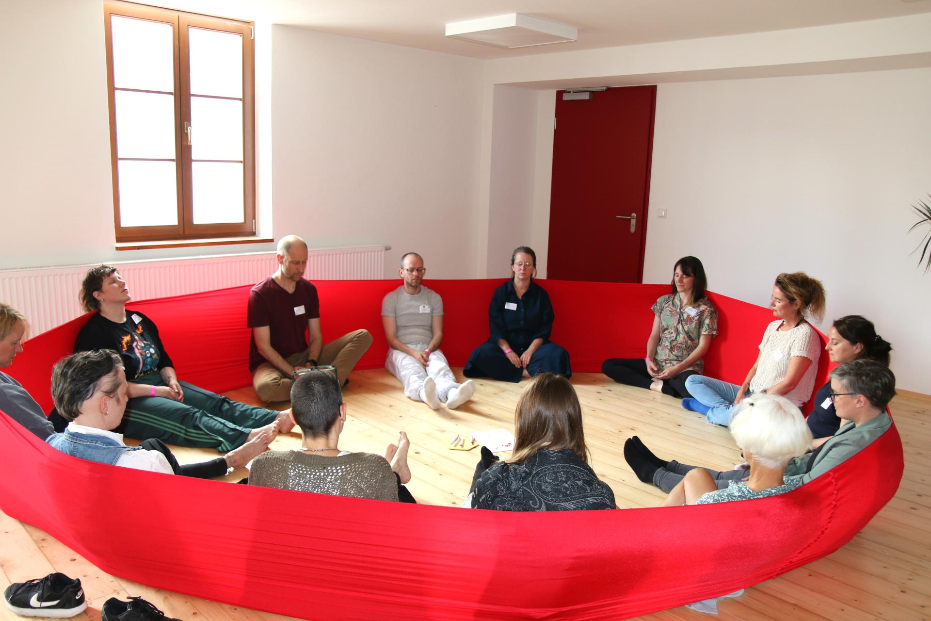 Group of 13 participants connected by a red scarf at the workshop “Embodied experiences of power(lessness)”