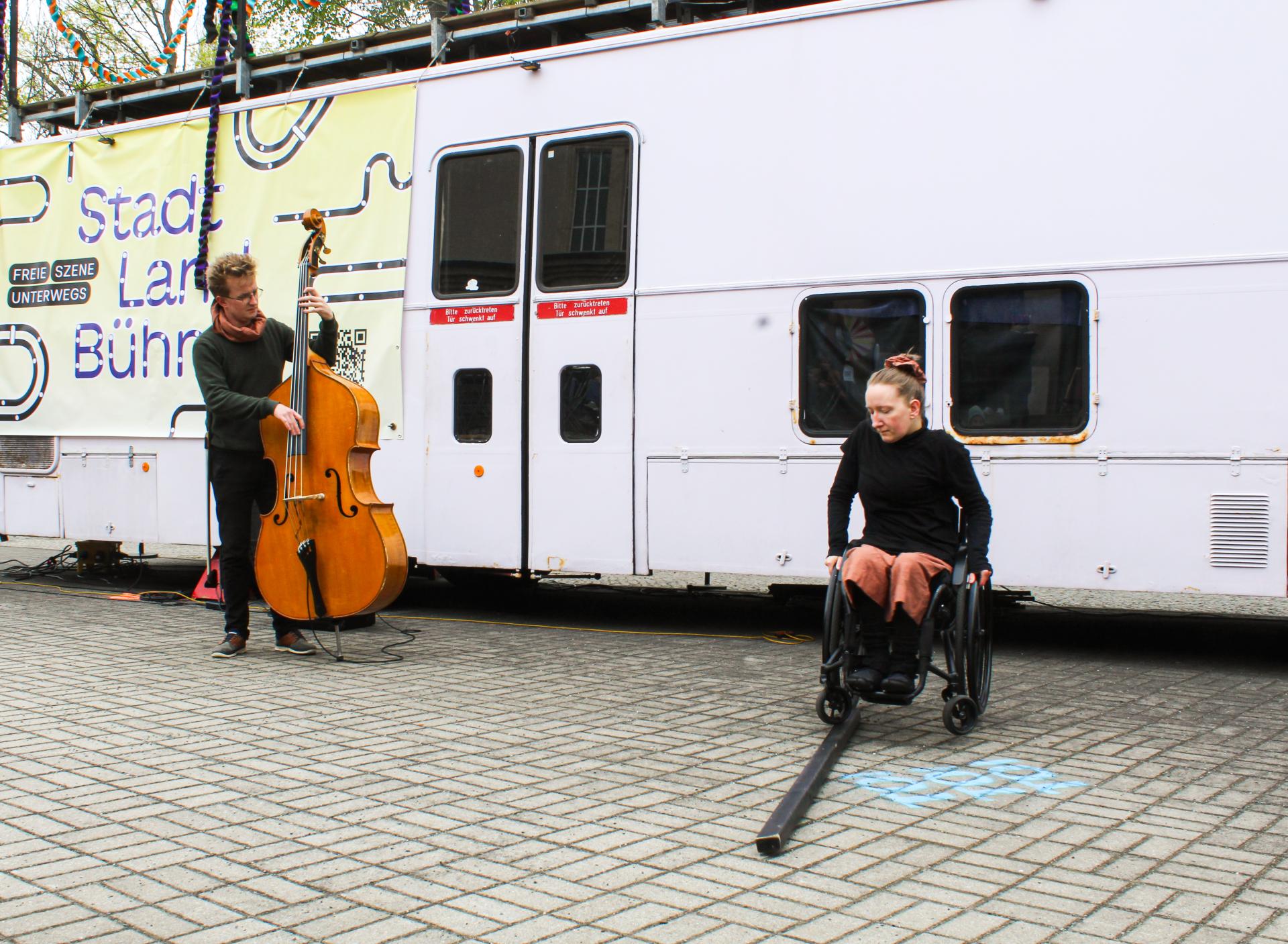 Two performers with a double bass and a wooden wedge, balancing