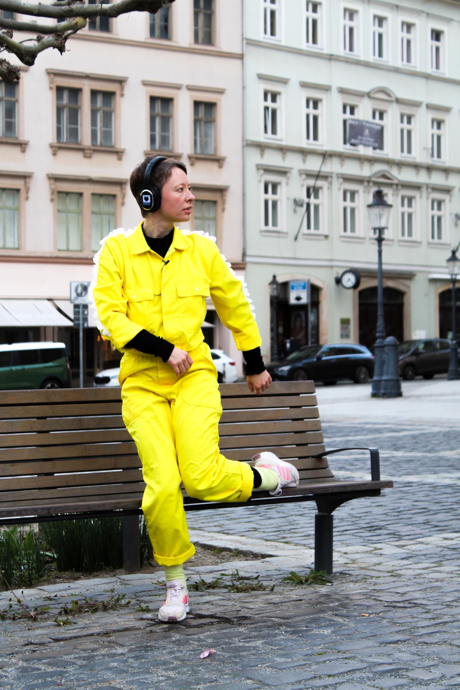 A performer in a yellow full-body suit leaning against a bench