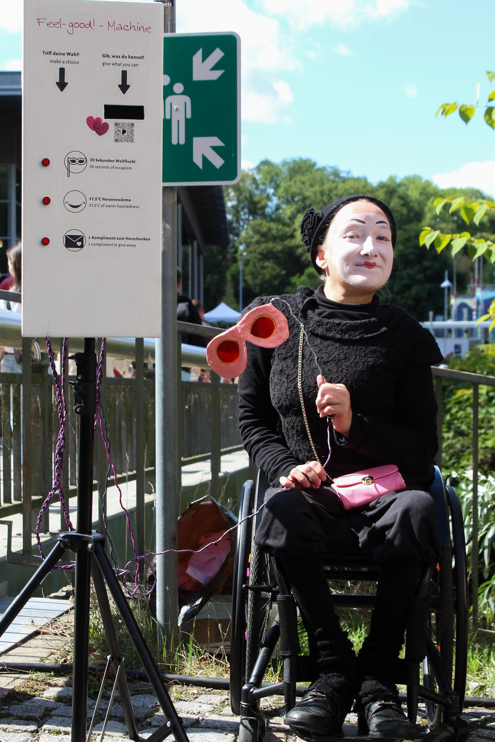 A performer in a wheelchair with her face painted white smiles at the camera