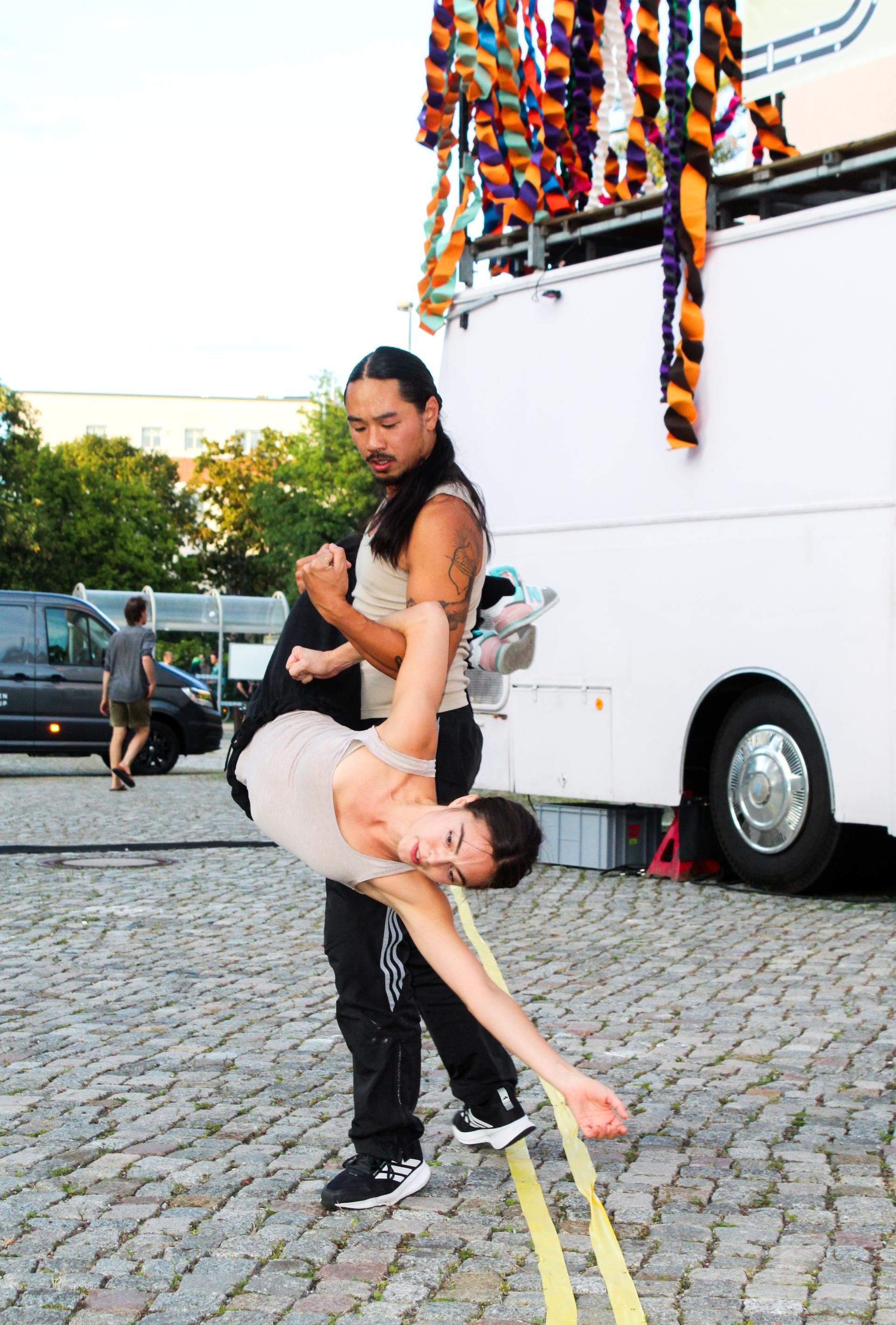 A male dancer performs a lift with a female dancer in front of a decorated vintage bus