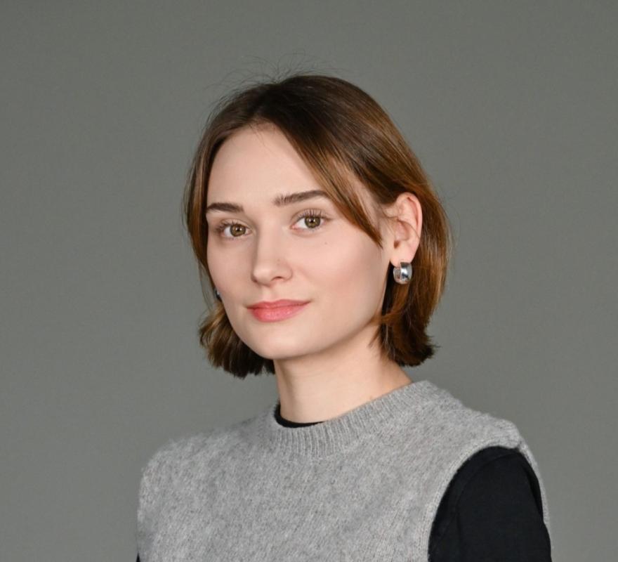 Sarah Biering Portrait of Sarah Biering with open brown hair and gray vest, looking frontally into the camera, in front of a light background