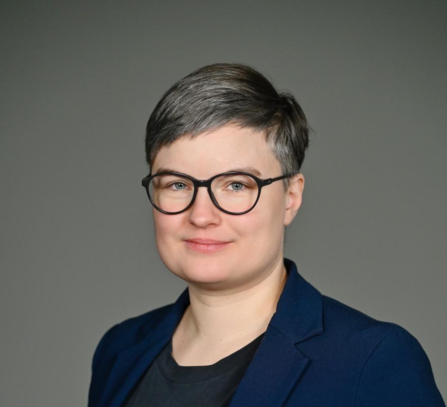 Anna Schinzel Portrait of Anna Schinzel with short hair and glasses, looking frontally into the camera, against a light background